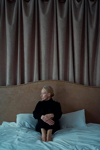 donna, seduto da solo, letto, sembra depresso, Outfit scuro, pensierosamente, le tende, Camera da letto, umore contemplativo, Scena indoor, solitudine