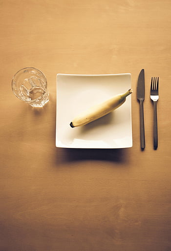 banán, bílá keramická deska, jasné sklenice na pití, Minimalistické stolování, příbory, čtvercová deska, dřevěný stůl, jednoduché jídlo, Nastavení snídaně, fotografování potravin, pohled shora