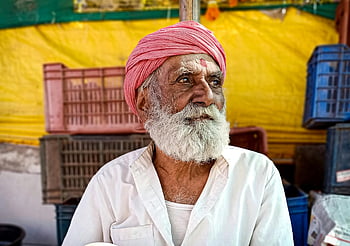 elderly Indian man, white button up shirt, turban, outdoor market, cultural heritage, beard, traditional attire, Indian culture, market scene, cultural representation, senior man