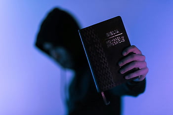 Bible, hooded figure, low-light, spirituality, mystery, holding Bible, religious book, dark setting, spiritual imagery, faith, religious symbolism