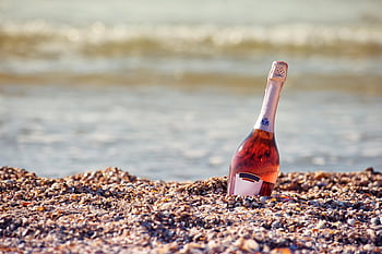 rose wine bottle, gray sand, sandy beach, seaside celebration, vacation theme, champagne bottle, beach scene, coastal setting, summer vibe, outdoor drink, beach party