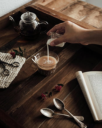 pouring milk, cup of coffee, cozy scene, open book, wooden tray, milk being poured, tea, spoons, flowers, teapot, reading