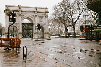 Marble Arch, London, rainy day, city buses, urban morning commute, historical landmark, wet pavement, traffic lights, cityscape, morning scene, reflections
