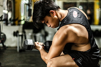 gym workout, young man, lifting dumbbell, strength training, focused exercise, black tank top, intense workout, gym environment, physical fitness, muscular build, workout routine