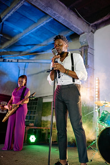 homme chantant, chemise blanche, pantalon gris, performance sur scène, jazz en direct, lumières colorées, chanteur, guitariste, immersion musicale, microphone, batterie
