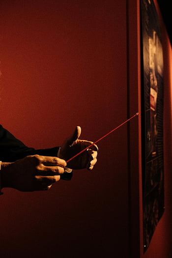 red pointer, hands holding, close-up, dark background, emphasizing direction, red stick, presentation tool, pointing device, educational tool, hand gesture, spotlight effect