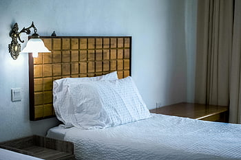 Kryt bílého povlečení, hnědý dřevěný boční stůl, dřevěná čelo, nástěnná lampa, Stylová ložnice, bílé ložní prádlo, dřevěný nábytek, ložnice dekor, Útulná ložnice, moderní ložnice, Vzhled interiéru