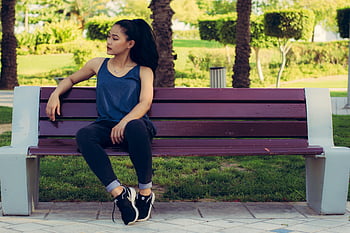 donna seduta, Panchina viola, parco soleggiato, giovane donna, momento di rilassamento, scena all'aperto, abbigliamento casual, sfondo verde, panchina del parco, postura rilassata, impostazione diurna