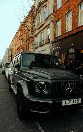 Mercedes 4x4, luxury SUV, city street, red brick buildings, Mercedes G-Class, urban setting, parked car, high-end vehicle, street scene, modern architecture, black SUV