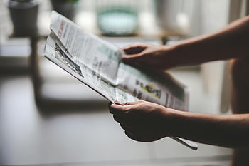 reading newspaper, hands holding newspaper, indoor environment, soft lighting, relaxed reading, close-up hands, newspaper articles, casual reading, indoor reading, soft-lit room, relaxed moment