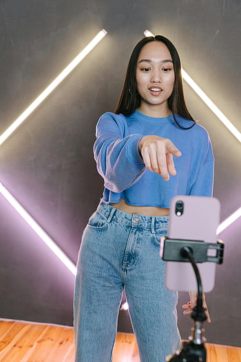 weibliche Content-Erstellerin, asiatische Frau, Streaming -Inhalt, Smartphone, Stativ, Modernes Setup, hinter den Kulissen, Vlogging, Inhaltserstellung, Neonlichter, Lässige Kleidung