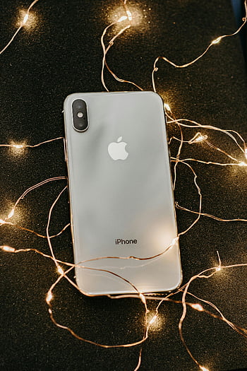 シルバーiphone x、 プリライトストリングライト、 洗練されたスマートフォン、 きらびやかな黒い表面、 温かい弦のライト、 現代の技術、 iphone x、 ストリングライト、 黒い表面、 暖かいライト、 テクノロジーショーケース