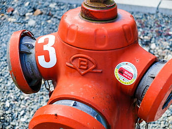 orange fire hydrant, red fire hydrant, fire hydrant number 3, Brabo fire hydrant, urban fire hydrant, emergency water source, street fire hydrant, public safety equipment, fire department equipment, outdoor fire hydrant, gravel background