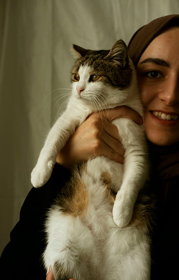 smiling woman, holding cat, adorable cat, cozy indoor setting, moment of joy, companionship, woman with cat, indoor photo, happy woman, pet owner, cat lover