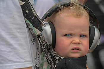 dítě se sluchátky, roztomilé dítě, velká sluchátka, venku, zvědavé miminko, dítě venku, dítě na sobě sluchátka, dítě s ochranou sluchu, dítě v nosítku, Zvědavý výraz