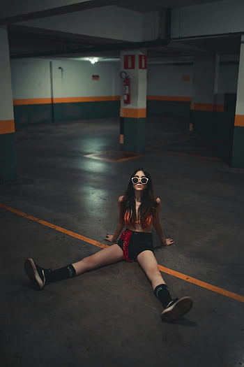 woman sitting, sunglasses, dimly lit, urban garage, trendy woman, casual pose, floor, garage interior, modern style, urban setting, casual fashion