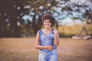 happy woman, curly hair, sunny outdoor park, blue scoop-neck top, blue denim bottoms, smiling woman, outdoor setting, casual outfit, natural light, park scene, cheerful mood