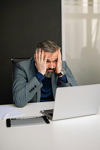 رجل متوتر،  طاولة المكتب،  يدا على وجهه،  شاشة الكمبيوتر المحمول،  رجل بالغ،  بدلة،  ضغوط العمل،  الإعداد المهني،  بيئة المكتب،  عمل الكمبيوتر،  إجهاد مكان العمل