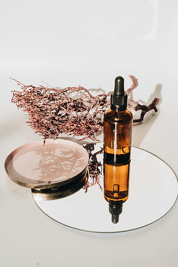 brun flaska, dropper, bärnstensfärgat glas, hudvårdsannonser, botanisk reflektion, spegel, eterisk olja, naturlig skönhet, kosmetisk produkt, minimalisk inställning, torkat sjögräs