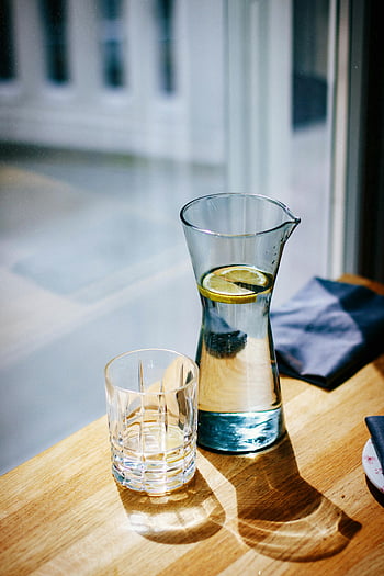 karafe vody, skleněná karafa, plátek citronu, prázdná sklenice, Slunečný dřevěný stůl, stíny, přirozené světlo, osvěžující nápoj, nastavení tabulky, stálý život, džbán na vodu