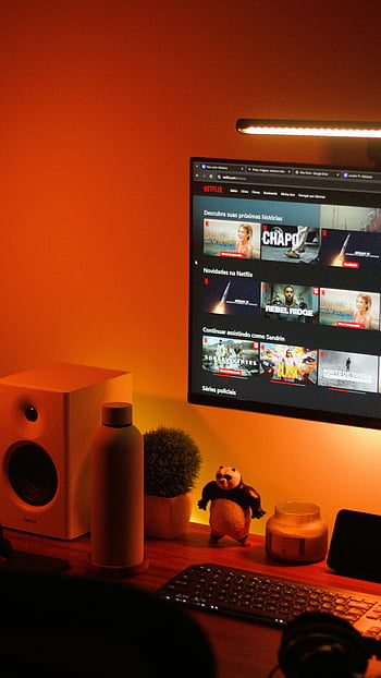 cozy home office, computer display, streaming service interface, warmly lit, home office setup, computer monitor, Netflix interface, desk setup, ambient lighting, office decor, speaker