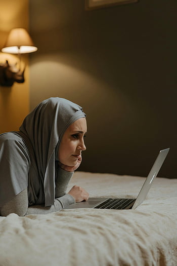 kvinne i hijab, Grå hijab, bruker bærbar PC, macbook air, eksternt arbeid, Koselig hjemmeinnstilling, muslimsk kvinne, ligger på sengen, hjemmekontor, jobbe hjemmefra, Bruk av bærbar datamaskin