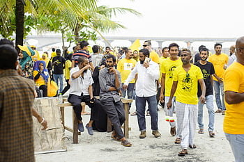 Gathering ao ar livre, unidade comunitária, homens sentados, grupo de pessoas, camisas amarelas, camisas brancas, evento animado, evento comunitário, evento ao ar livre, pessoas de amarelo, pessoas de branco