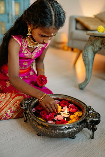 girl lighting tealight candle, young girl, traditional attire, Diwali, cultural celebrations, candles, flowers, festival, indoor setting, festive atmosphere, cultural tradition