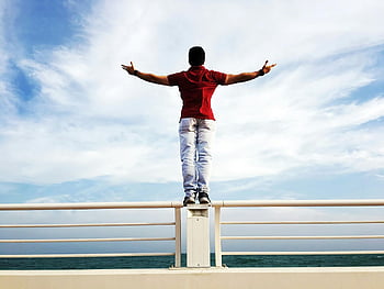 person raising hands, mid-air, gray steel railings, standing on railing, arms outstretched, clear sky, freedom, sea view, outdoor scene, balance, freedom symbol