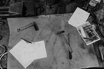 blacksmith workspace, black and white image, hand tool, gray concrete floor, design sketches, workshop tools, blacksmith tools, metalworking tools, workshop environment, black and silver tool, blacksmith's workspace