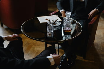 men in black suits, armchairs, round table, pitcher, glass, whiskey, cigars, classic ambiance, bar table, two men, suits