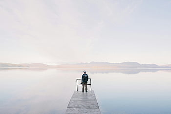 man wearing jacket, wooden docks, body of water, solitary traveler, serene water view, standing on dock, enjoying view, calm water, peaceful scene, outdoor scene, nature photography