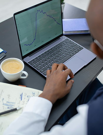 személy használ laptop, pénzügyi diagramok, irodai környezet, kávé, jegyzetfüzet, szakmai elemzés, laptop képernyő, íróasztal, Üzleti elemzés, pénzügyi adatok