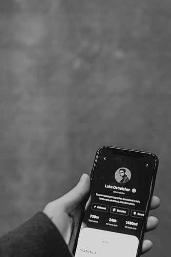 greyscale photo, person holding smartphone, close-up hand, smartphone display, profile interface, monochromatic color scheme, black and white, mobile phone, digital interface, social media profile, technology