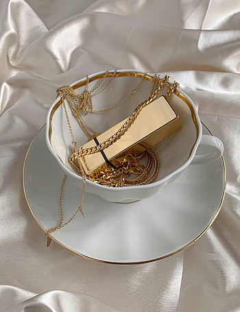 gioielleria in oro, tazza bianca, piattino, Tessuto di raso lucido, composizione elegante, catene d'oro, scatola d'oro, accessori di lusso, gioielleria, tazza di tè, display decorativo