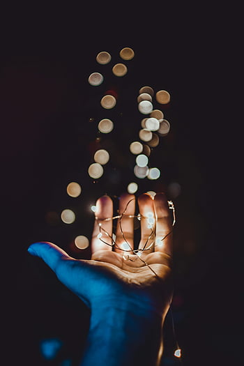 hand, glowing string lights, bokeh effect, close-up, dark background, warm glow, soft focus, string lights, bokeh, hand holding lights, bokeh background