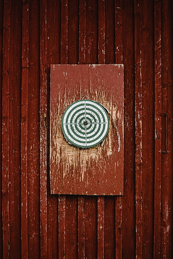 dartboard, red wall, distressed wood, rustic aesthetic, hanging dartboard, wooden wall, red wooden wall, intriguing aesthetic, dartboard on wall, vintage dartboard, red paint