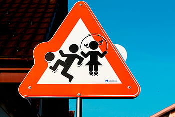 children playing sign, road safety, triangular sign, bright blue sky, red and white sign, child safety, warning sign, traffic sign, pedestrian safety, play area sign, caution sign