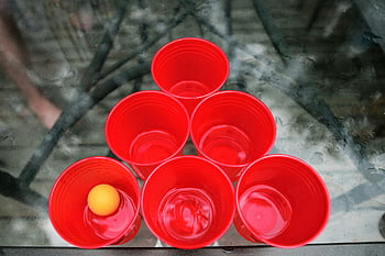 Beer Pong, red plastic cups, yellow ping pong ball, outdoor game, top view, party game, drinking game, social activity, outdoor setup, red cups, yellow ball