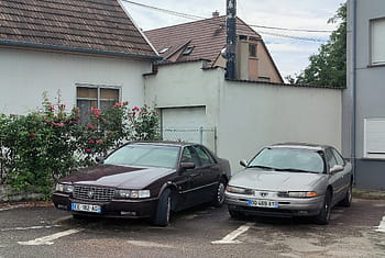 Cadillac Seville Sts, วิสัยทัศน์ของไครสเลอร์, รถยนต์ที่จอดอยู่, ย่านที่อยู่อาศัย, แผ่นป้ายทะเบียนยุโรป, รถโบราณ, เคียงบ่าเคียงไหล่, ที่จอดรถกลางแจ้ง, รถคลาสสิก, พุ่มไม้ดอกไม้, บ้านสีขาว