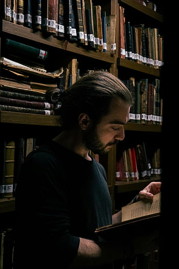 bearded man, reading, library, tall bookshelves, dimly lit, engrossed in reading, intellectual, quiet setting, academic atmosphere