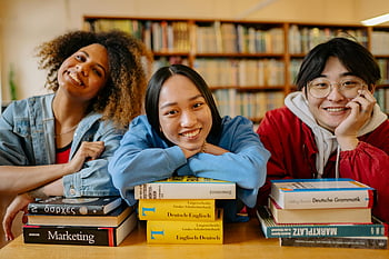 smiling students, library, studying, stacks of books, three students, learning environment, books on table, engaged students, educational setting, diverse students, library scene
