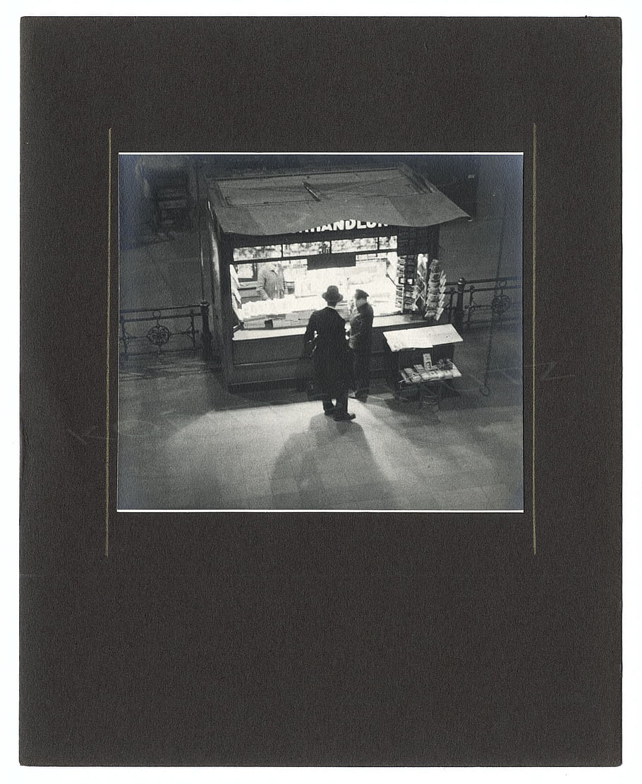 train station, kiosk, people, newspapers, vintage, black and white, urban, street scene, architecture, candid, daily life