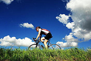 man riding road bike, cyclist, sportswear, bright blue sky, clouds, outdoor cycling, grassy field, active lifestyle, road cycling, fitness, recreation