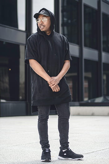 man met capuchon, Zwarte vrijetijdskleding, stedelijke levensstijl, modieuze jongeman, buitenhouding, zelfverzekerde pose, zwarte hoodie, Street Style, moderne mode, Vrijetijdsoutfit, stedelijke mode