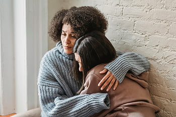 sad multiracial women, emotional embrace, comfort and support, indoors, friends hugging, home setting, multiracial friendship, emotional support, indoor hug, supportive friends, multiracial women hugging