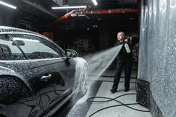 woman washing car, pressure washer, black car, indoor car wash, car cleaning, high pressure cleaning, car detailing, auto care, vehicle maintenance, car wash service, water spray