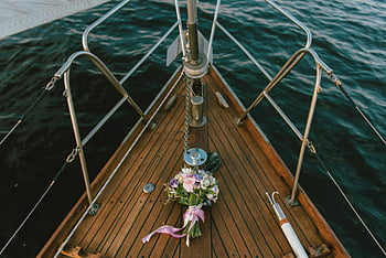 bridal bouquet, white and purple flowers, brown wooden boat, yacht deck, body of water, serene nautical theme, ocean view, wedding flowers, floral arrangement, boat deck, water backdrop