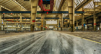 industrial warehouse, empty building, concrete interior, metal structures, wide view, gray concrete, cranes visible, factory space, large facility, structural elements