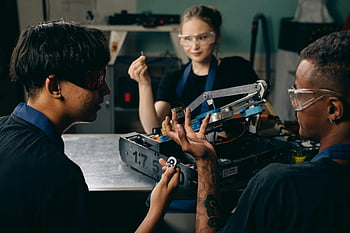 Freunde sitzen, Tabelle, Ingenieure, Indoor -Workshop, Robotermontage, Programmierung, Zusammenarbeit, Schutzbrillen, Zusammenspiel, Technologie, Projekt